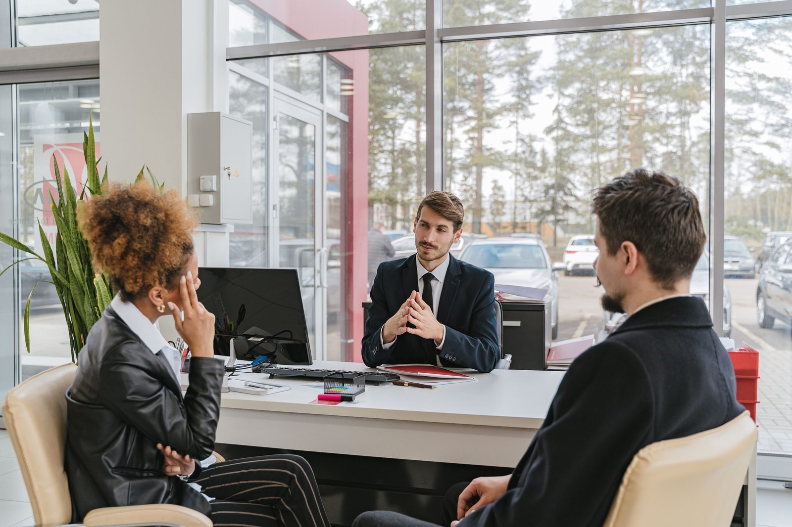 A finance manager reviewing paperwork with customers at his desk in a dealership office